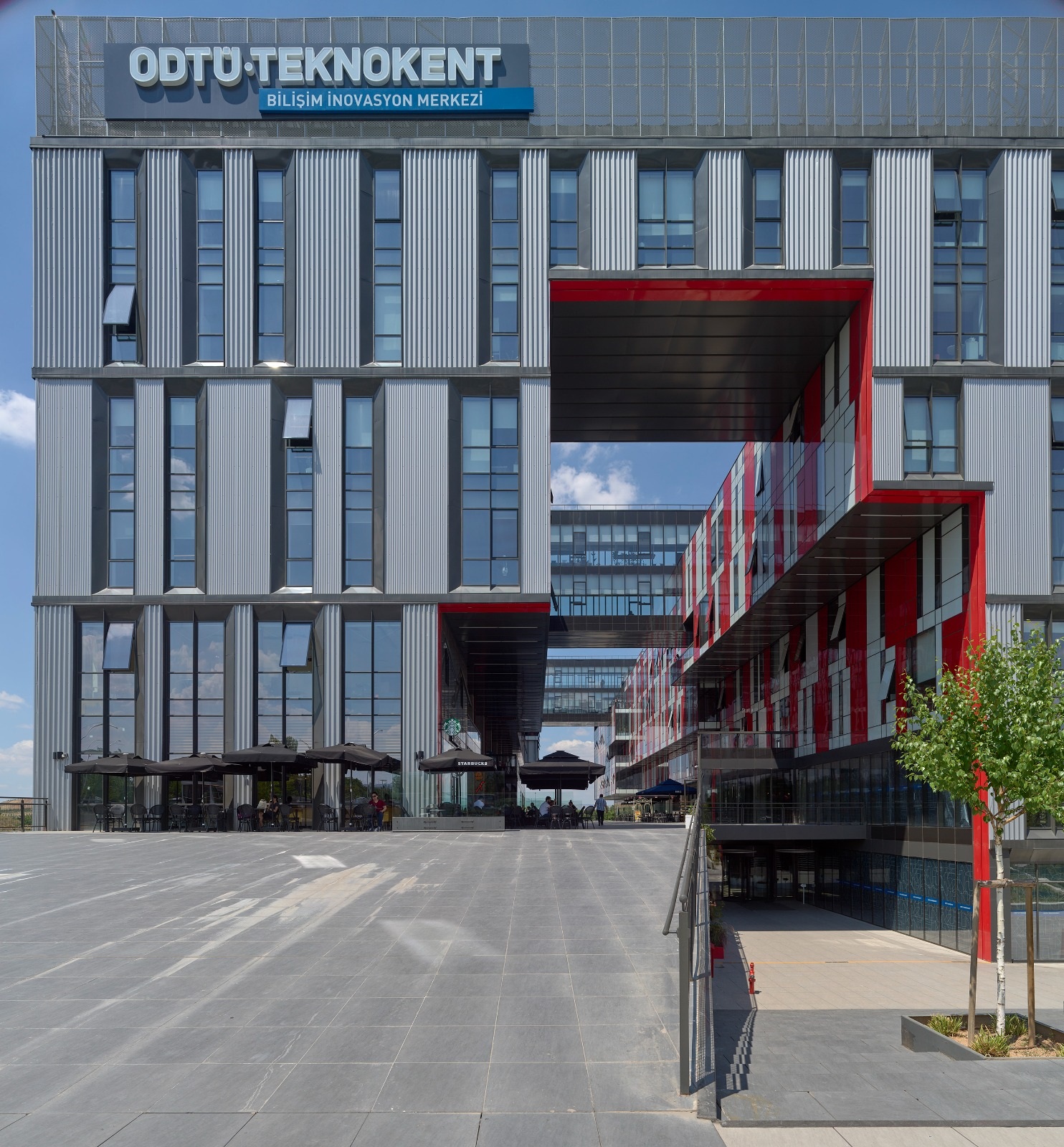 The ICT Innovation Centre’s silver facade and red-framed passage at ODTÜ TEKNOKENT