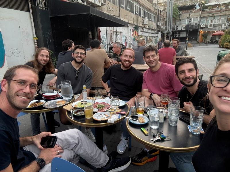 Ofer Amitai and colleagues sharing food and drinks at outdoor tables in Tel Aviv
