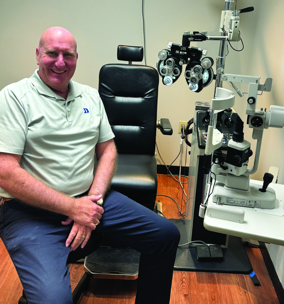 Optometrist John Scibal seated beside eye-examination equipment in his practice