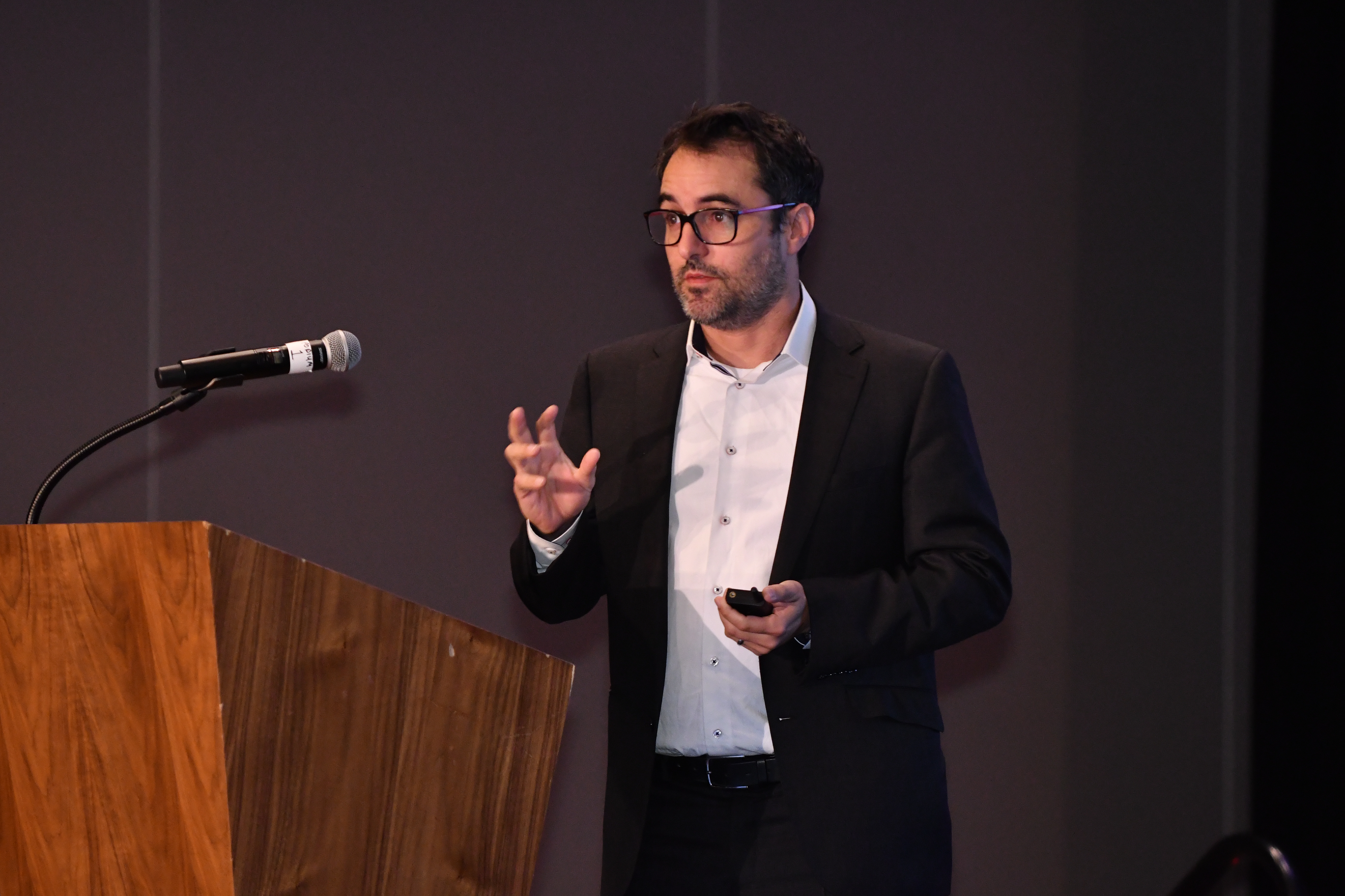 Ohad Samet speaking at a podium, holding a presentation remote