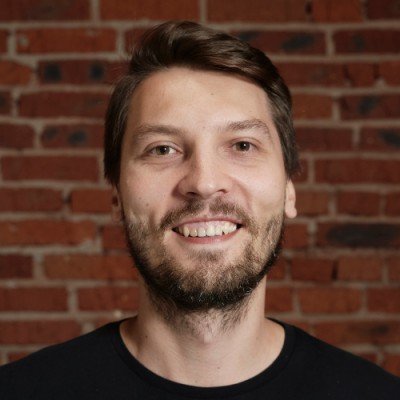 Oleg Shardin smiling in front of a brick wall