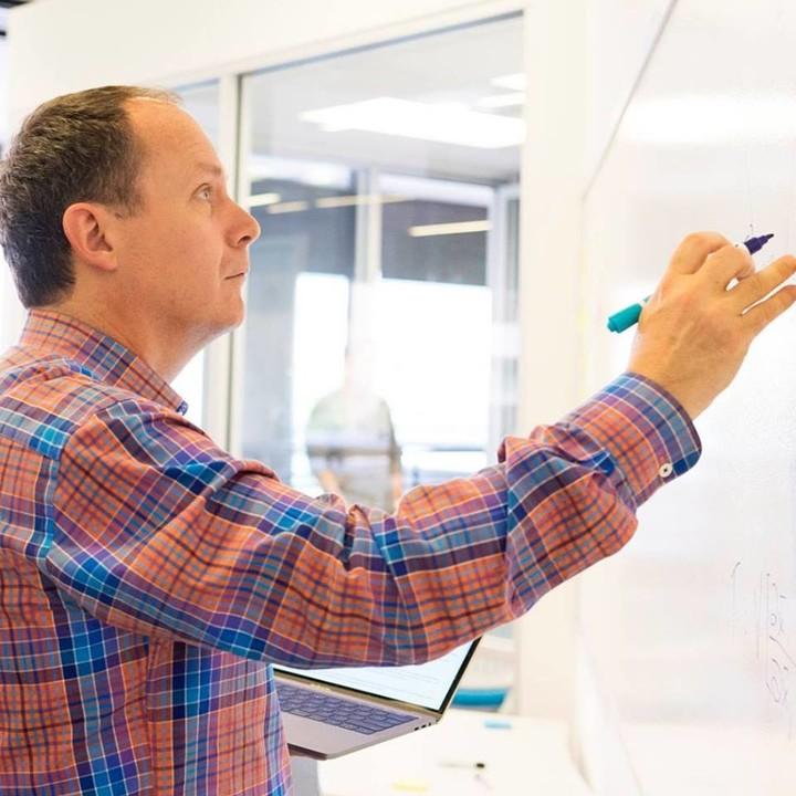 Olin Hyde holding markers and writing on a whiteboard in an office