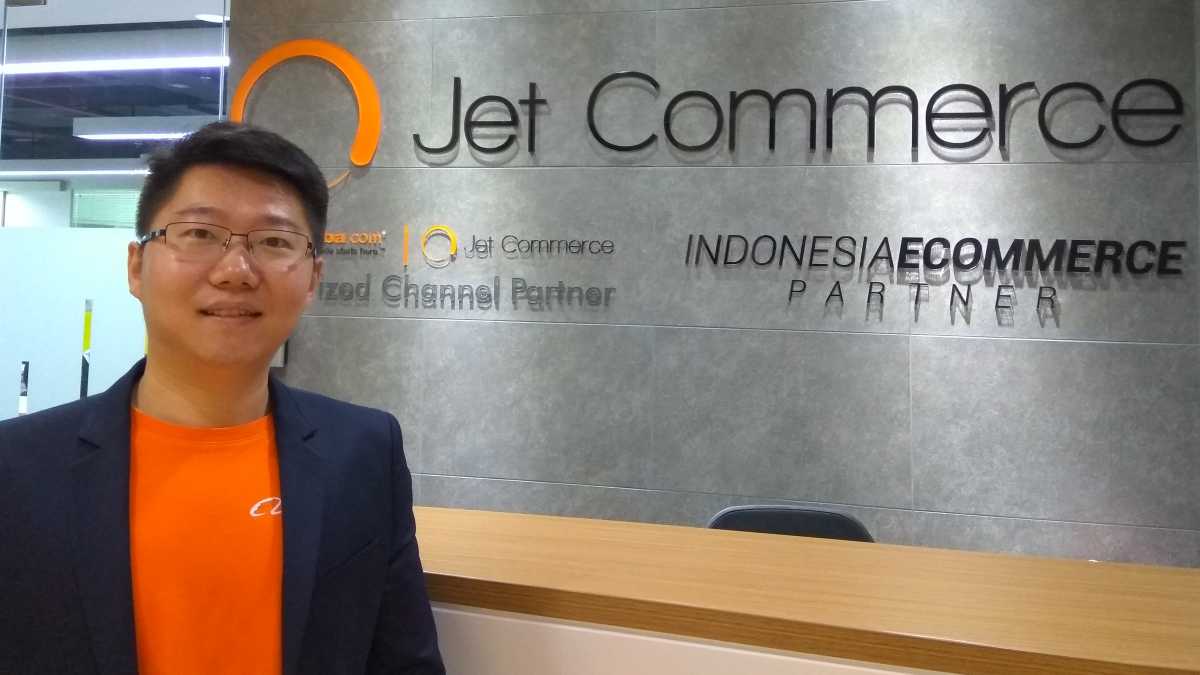 Oliver Yang standing at Jet Commerce’s office, wearing an orange shirt and navy jacket