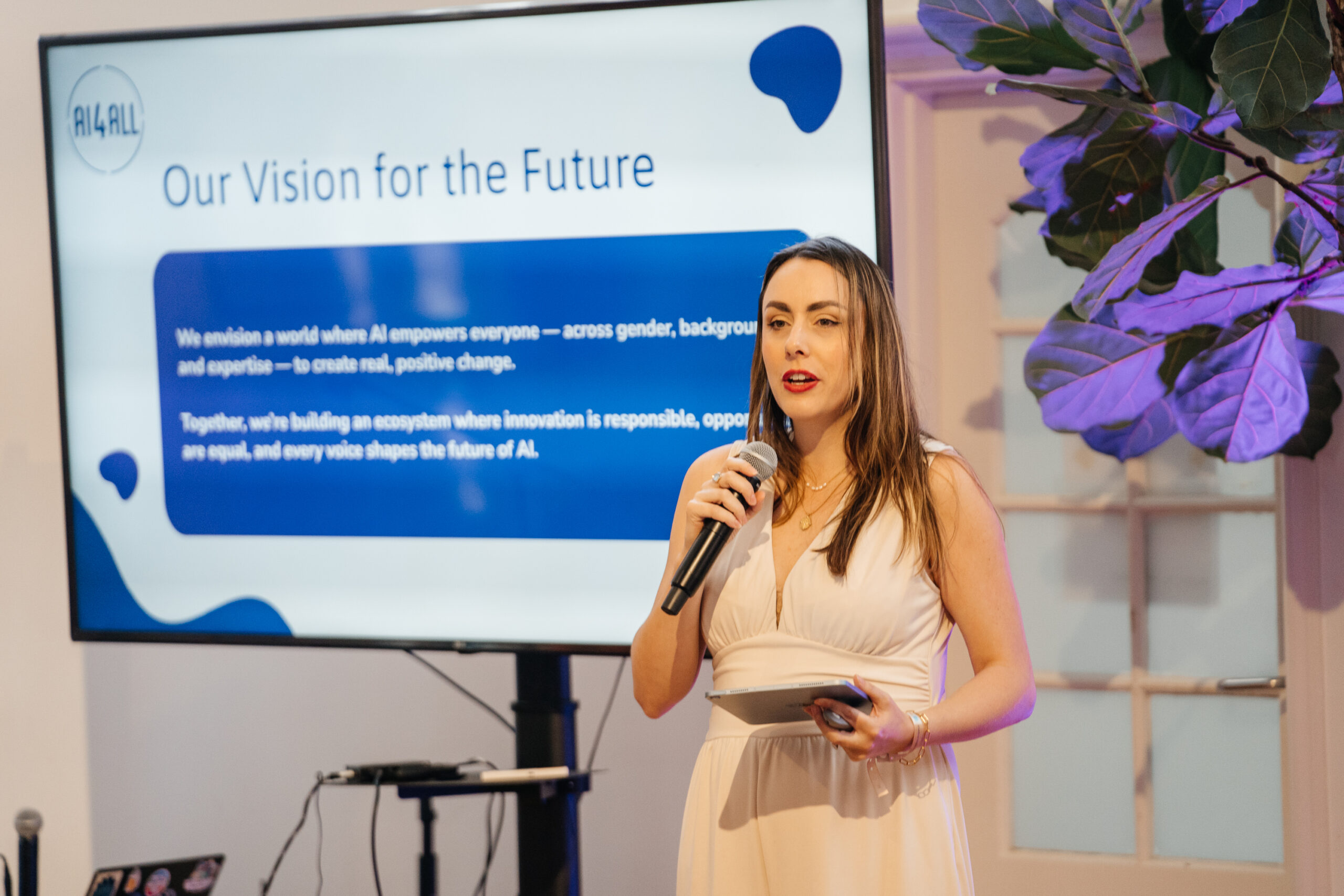 Oliviana Bailey speaking into a microphone beside an AI4ALL presentation
