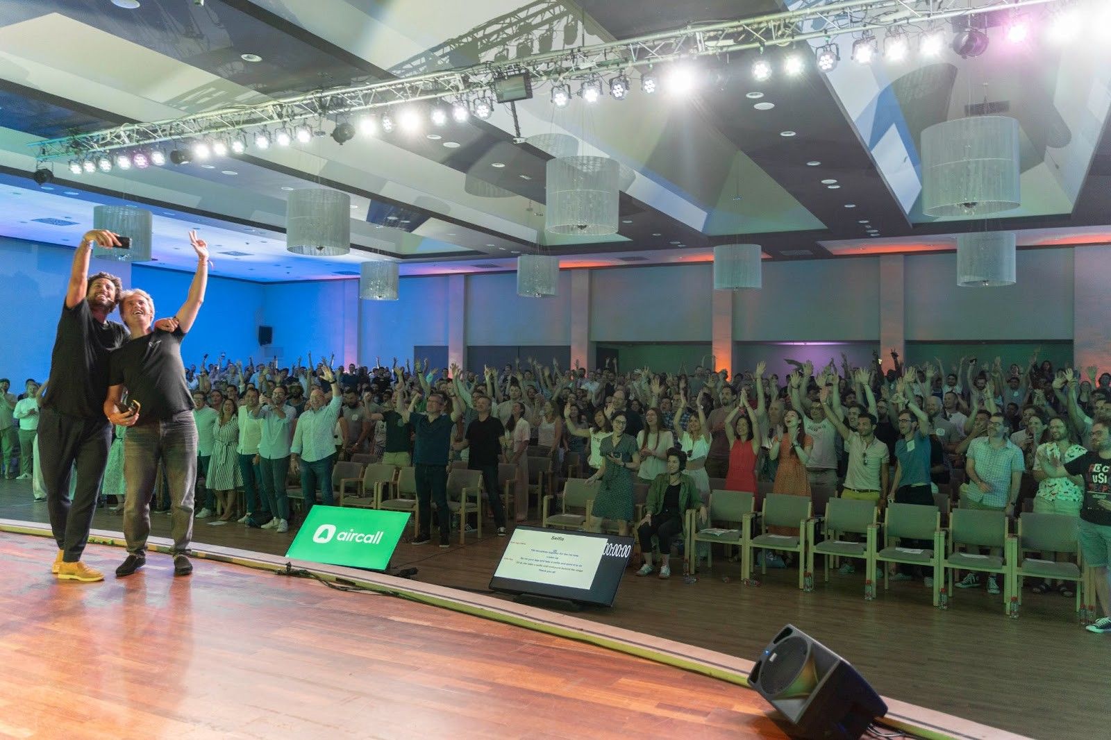 Olivier Pailhes and Jonathan Anguelov taking a selfie on stage with Aircall colleagues at the 2022 company offsite