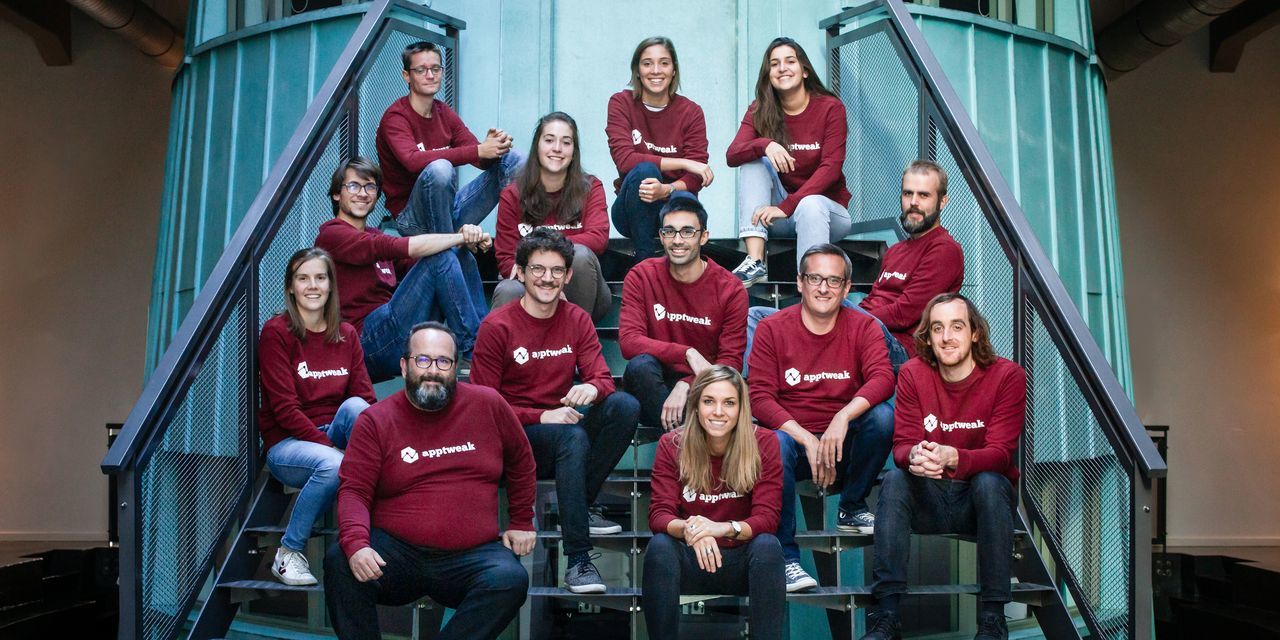 Olivier Verdin seated with AppTweak colleagues on an industrial staircase, wearing matching burgundy company sweatshirts