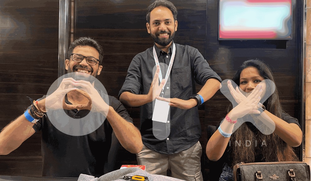 Three people in an OLX India workplace photograph make the letters O, L and X with their hands.