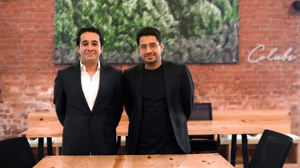 Omar and Ali Shah standing together in a COLABS workspace with exposed brick and wooden tables