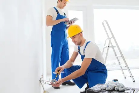 Two maintenance workers, one recording information on a tablet while another works on wiring