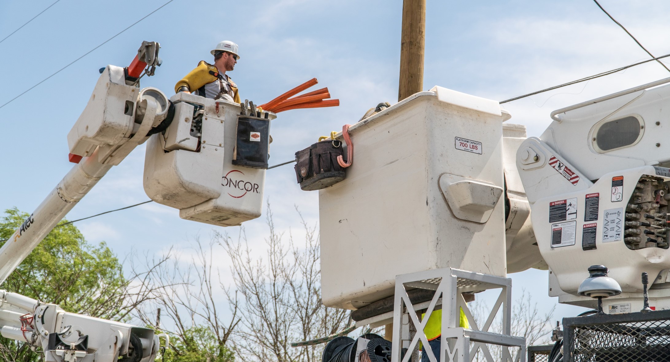 An Oncor field worker in a bucket lift beside overhead electricity lines