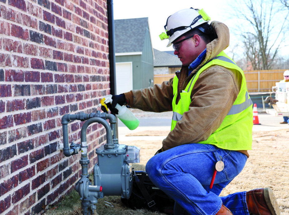A field employee in a hard hat and safety vest working at a residential natural gas meter