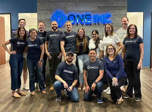 One Inc employees gathered in front of an illuminated company sign