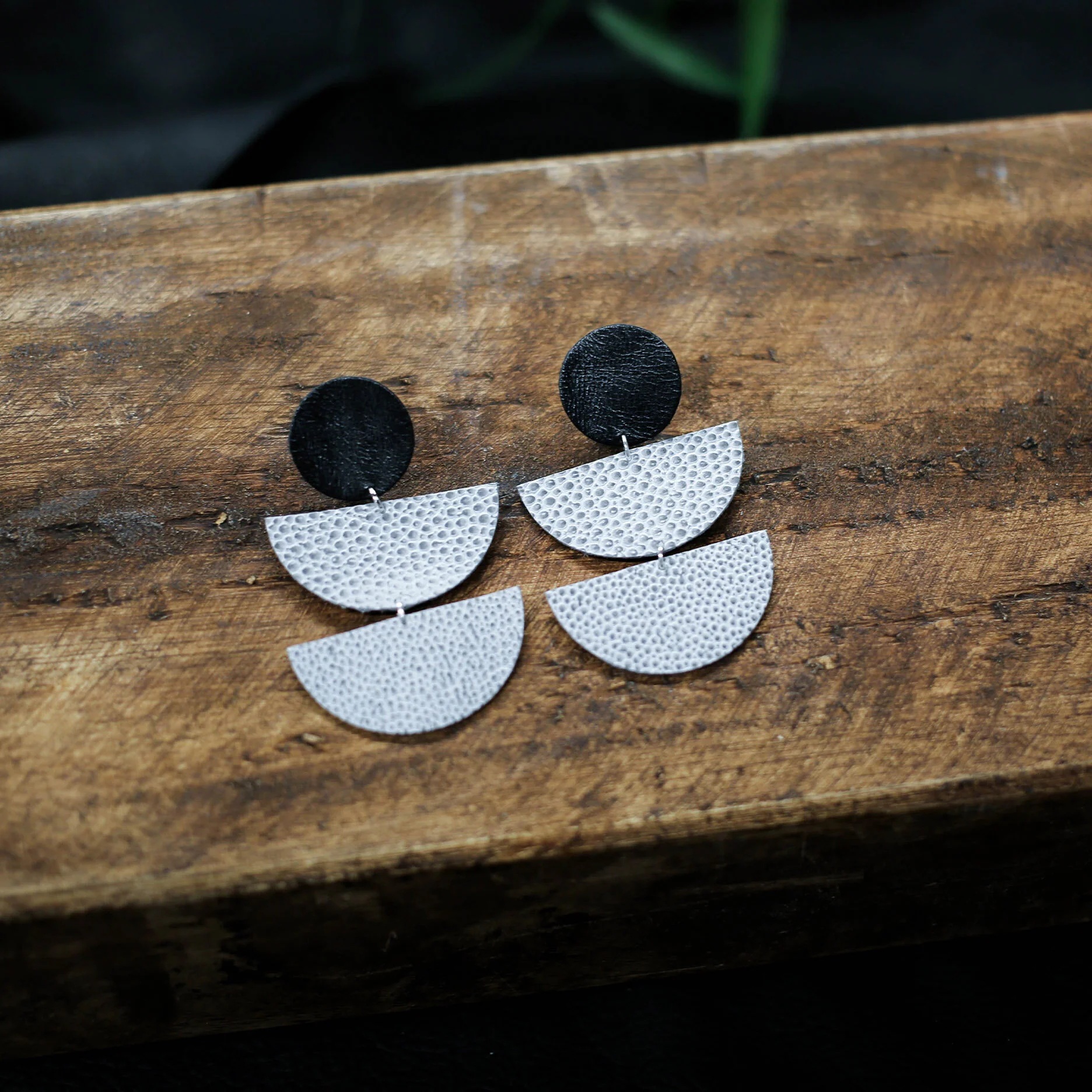 Geometric black and silver-toned earrings displayed on wood in the Close the Loop collection
