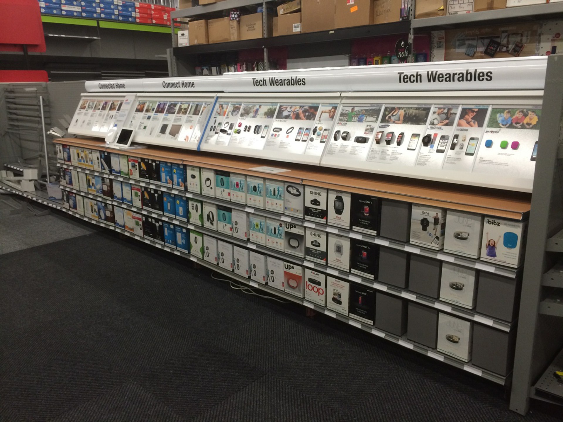 A long OnQ wearable-technology display with watches above stocked product shelves