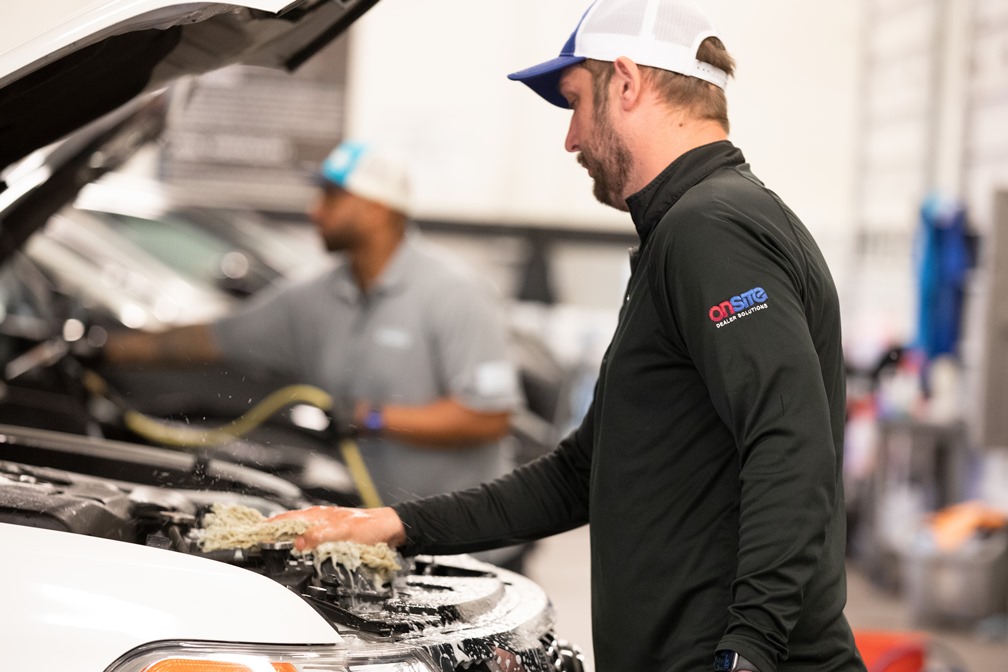 OnSite employees cleaning a vehicle with its hood raised in a dealership work bay