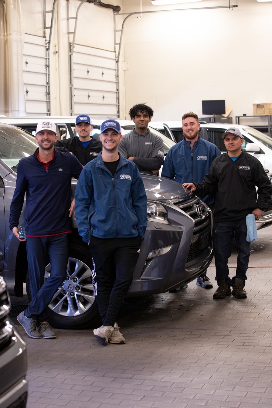 Six members of the OnSite team standing with vehicles inside a dealership bay