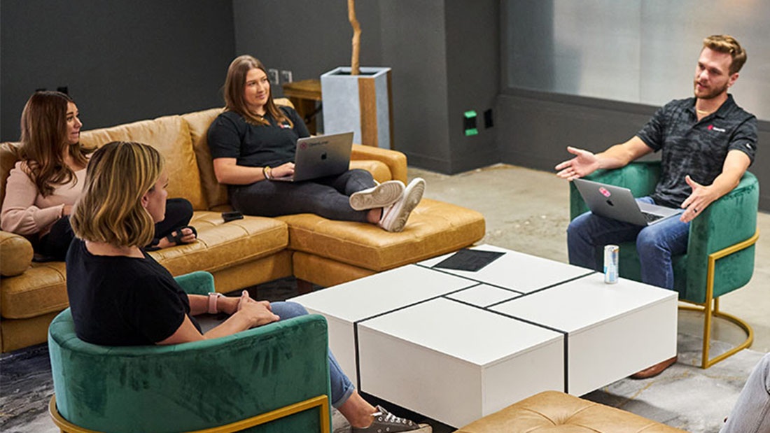 Four colleagues with laptops talking in an OpenLoop workplace lounge