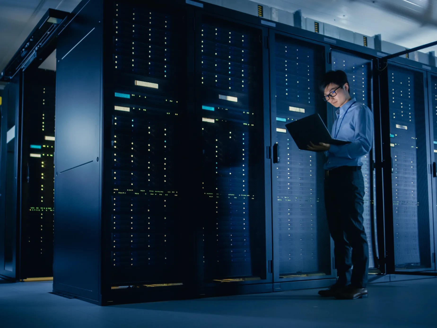 Engineer with a laptop working among server racks in a data center