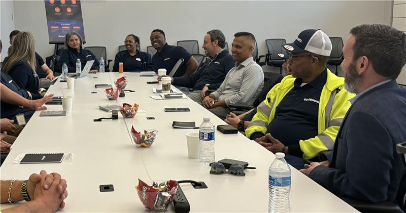 Optimum CEO Dennis Mathew meets employees around a conference table.