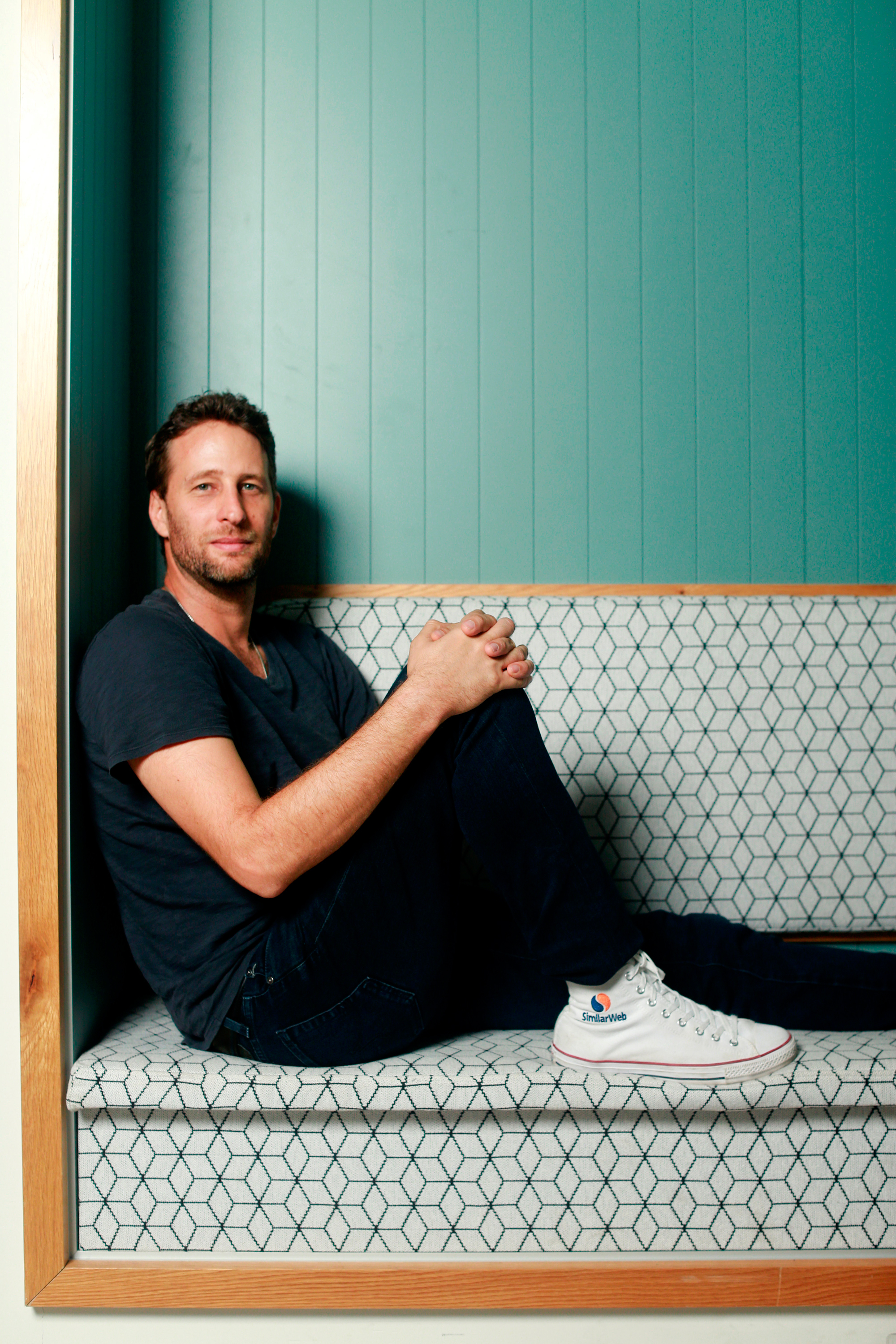 Or Offer seated in a patterned booth, wearing Similarweb-branded sneakers