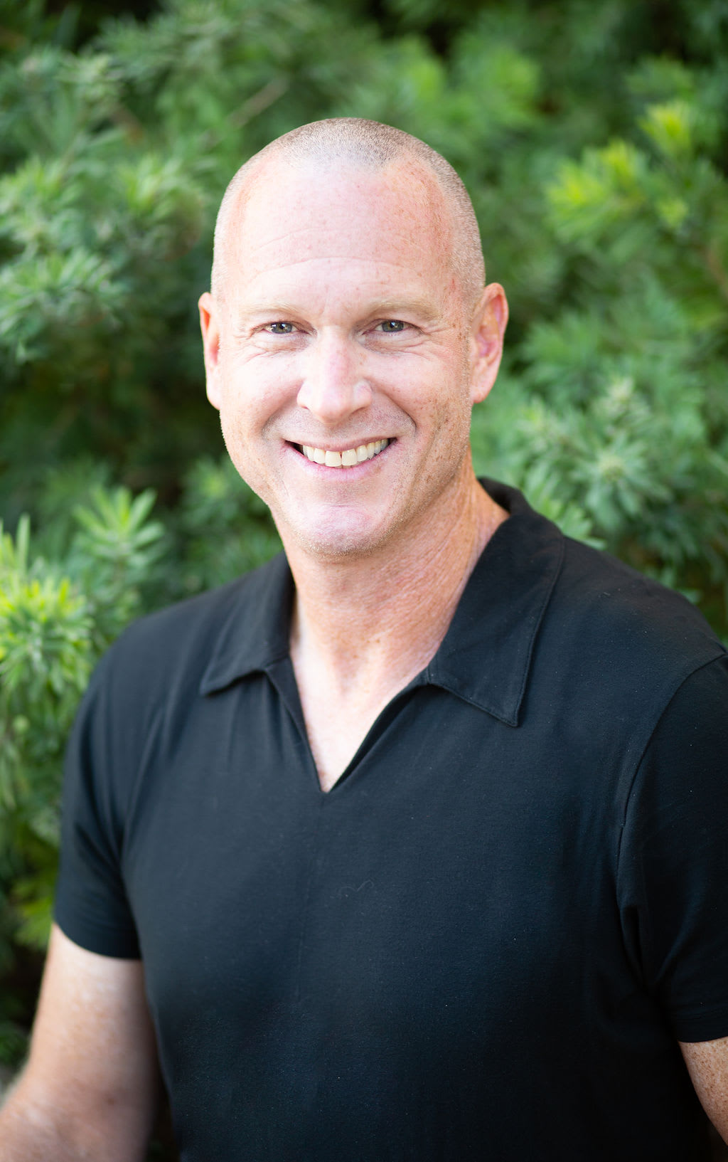 Oren Zaslansky in a black shirt, photographed outdoors against green foliage