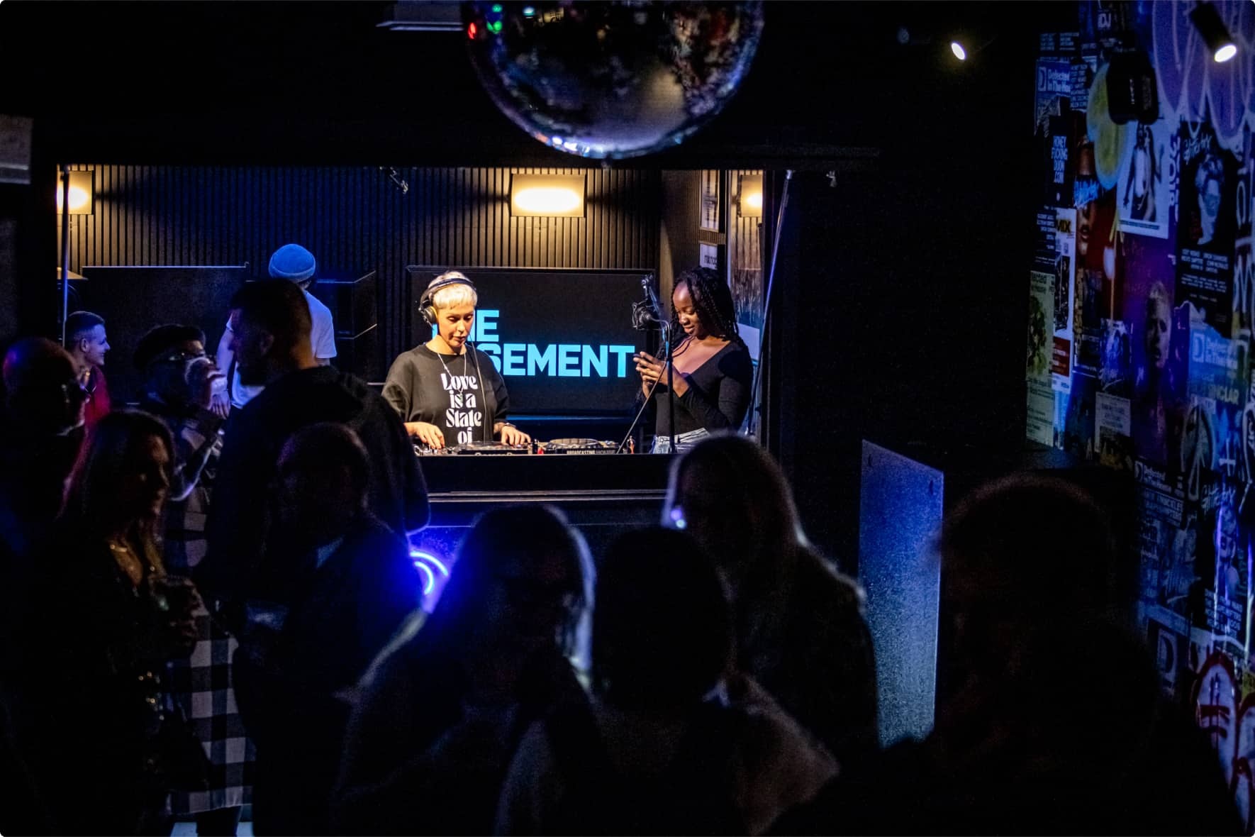A DJ and vocalist perform beneath a disco ball at an Orfium get-together