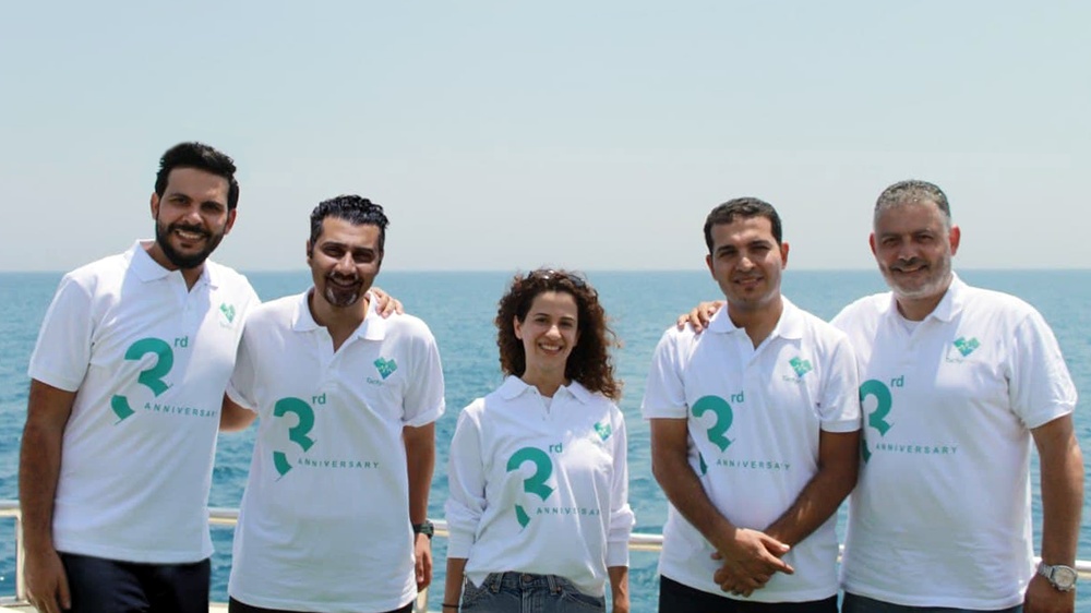 Five members of the TachyHealth team in matching third-anniversary polo shirts beside the sea