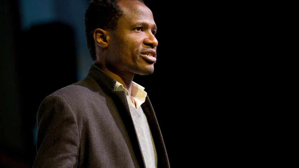 Osh Agabi speaking on a dark stage