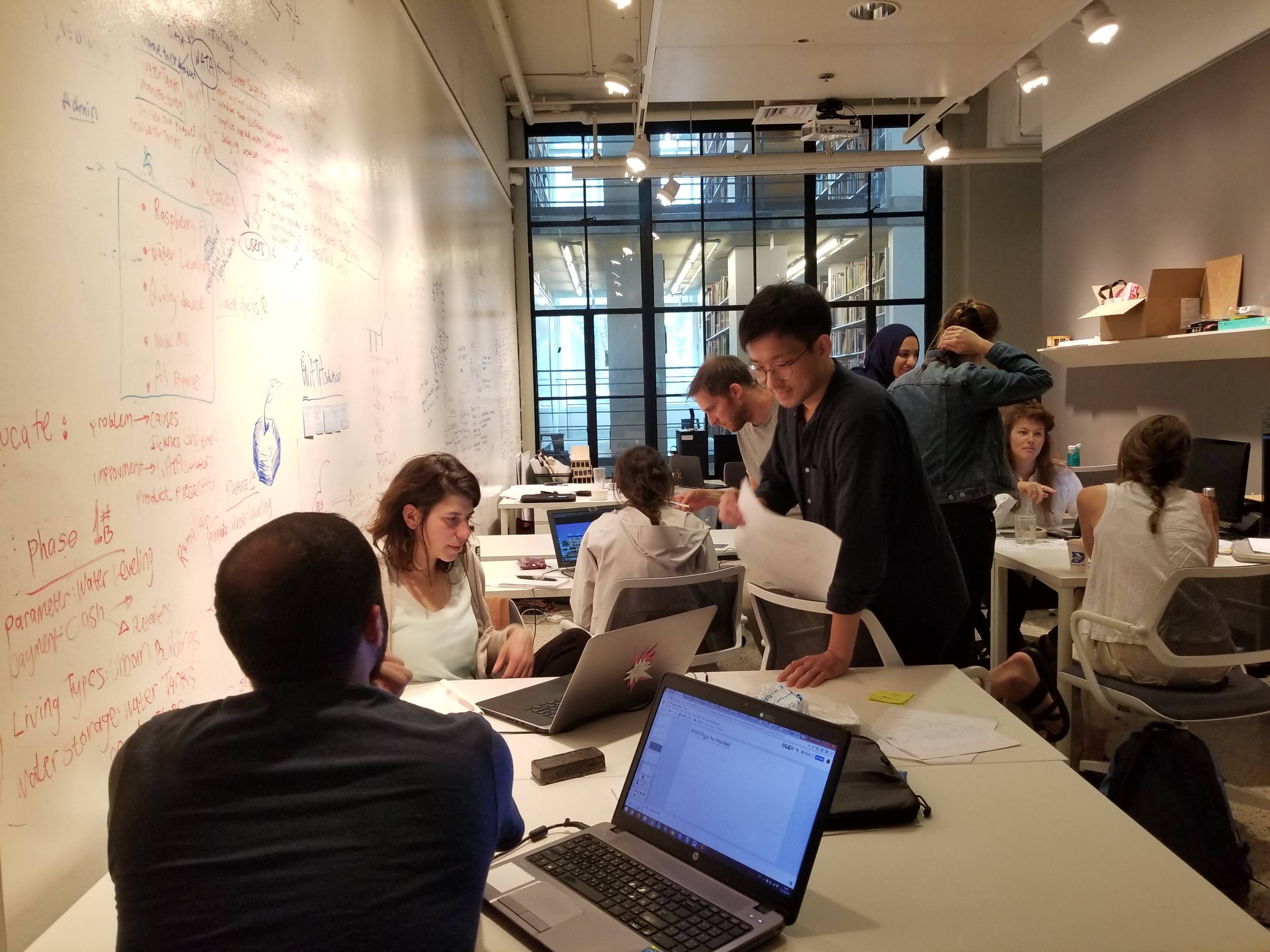 OGS fellows and MIT student interns working at tables beside a wall of handwritten plans