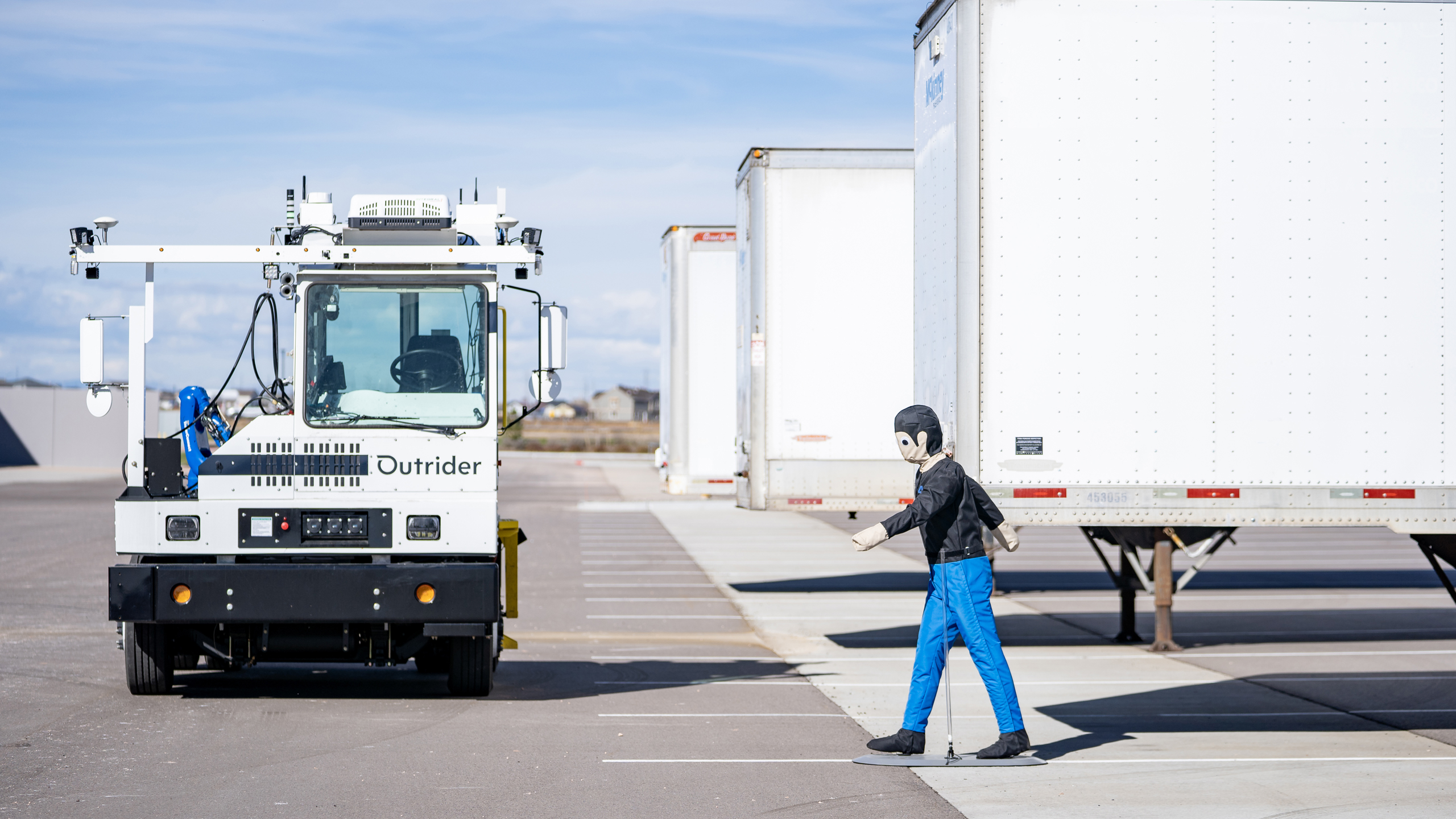 An Outrider autonomous electric yard truck approaches a pedestrian test dummy in a distribution yard