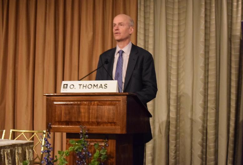Owen Thomas speaking behind a wooden lectern at a real estate symposium