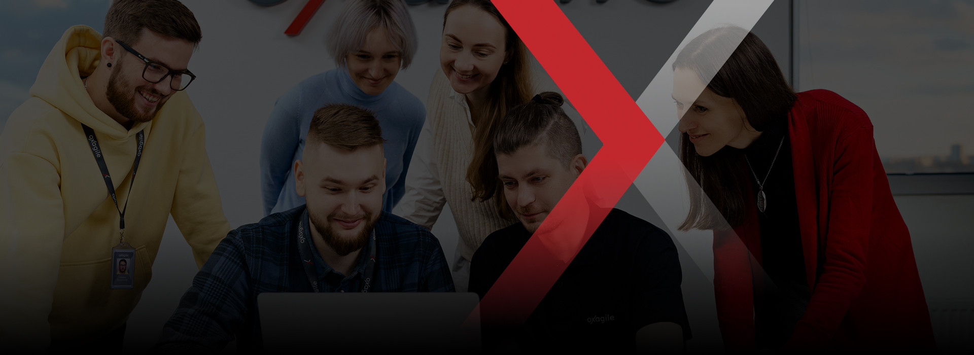 Oxagile colleagues gathered around a laptop in a company photograph with a red graphic overlay