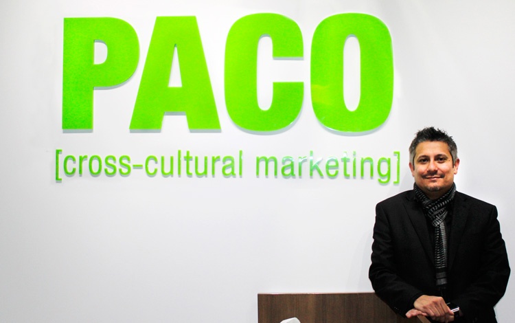 Ozzie Godinez standing beside PACO’s green cross-cultural marketing office signage
