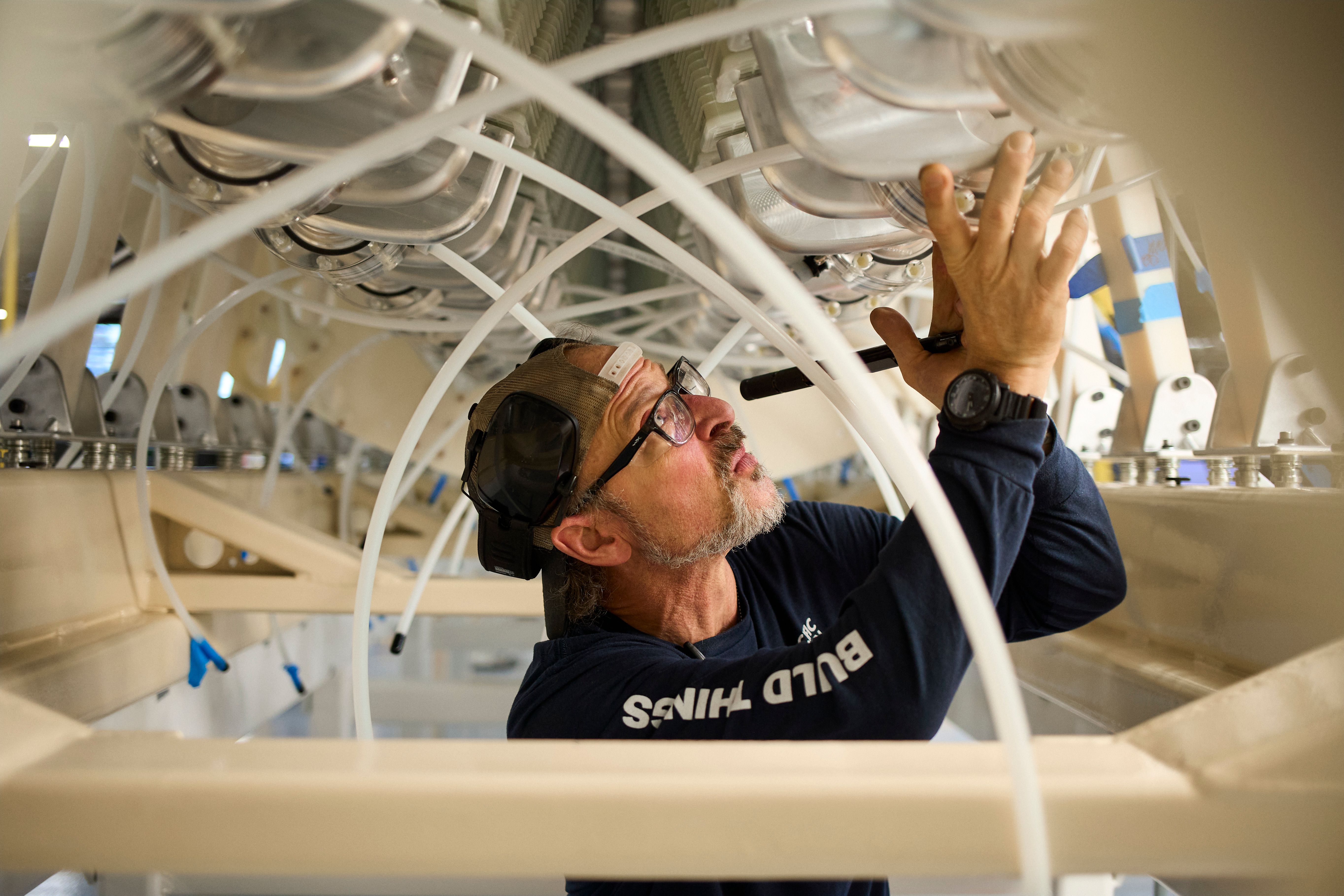 A Pacific Fusion technician working among the tubes and components of a pulser module in San Leandro