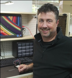 Packy Hyland at a workbench with a computer monitor, drawers and electronic components
