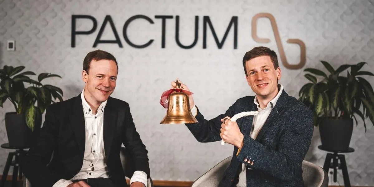 Two Pactum co-founders with a brass bell in front of the company name