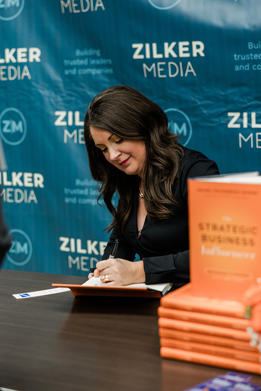 Paige signing a copy of The Strategic Business Influencer beside a stack of orange books