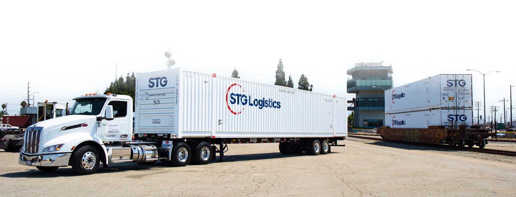 STG Logistics truck beside stacked intermodal containers and a rail line