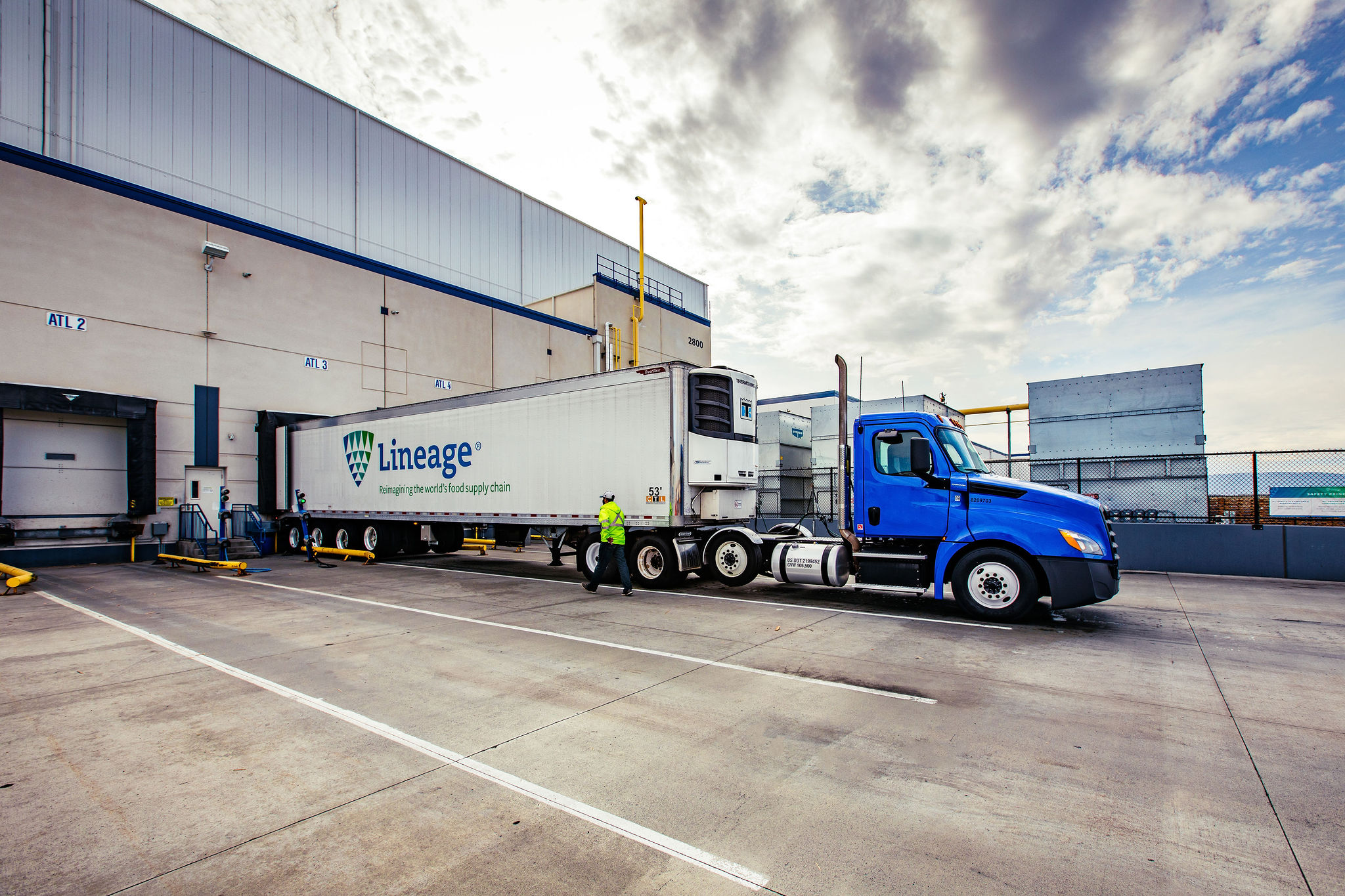 A refrigerated Lineage trailer and blue tractor at a warehouse loading dock
