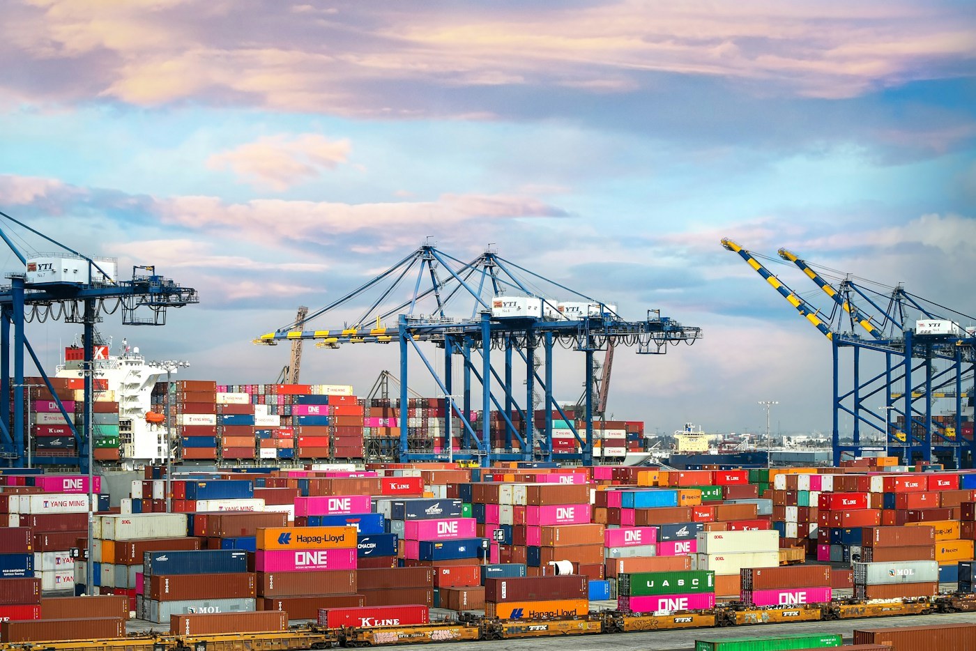 Rows of colorful shipping containers beneath blue port cranes
