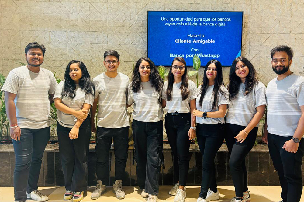 Eight Panamax Infotech team members standing together beneath a screen presenting WhatsApp banking