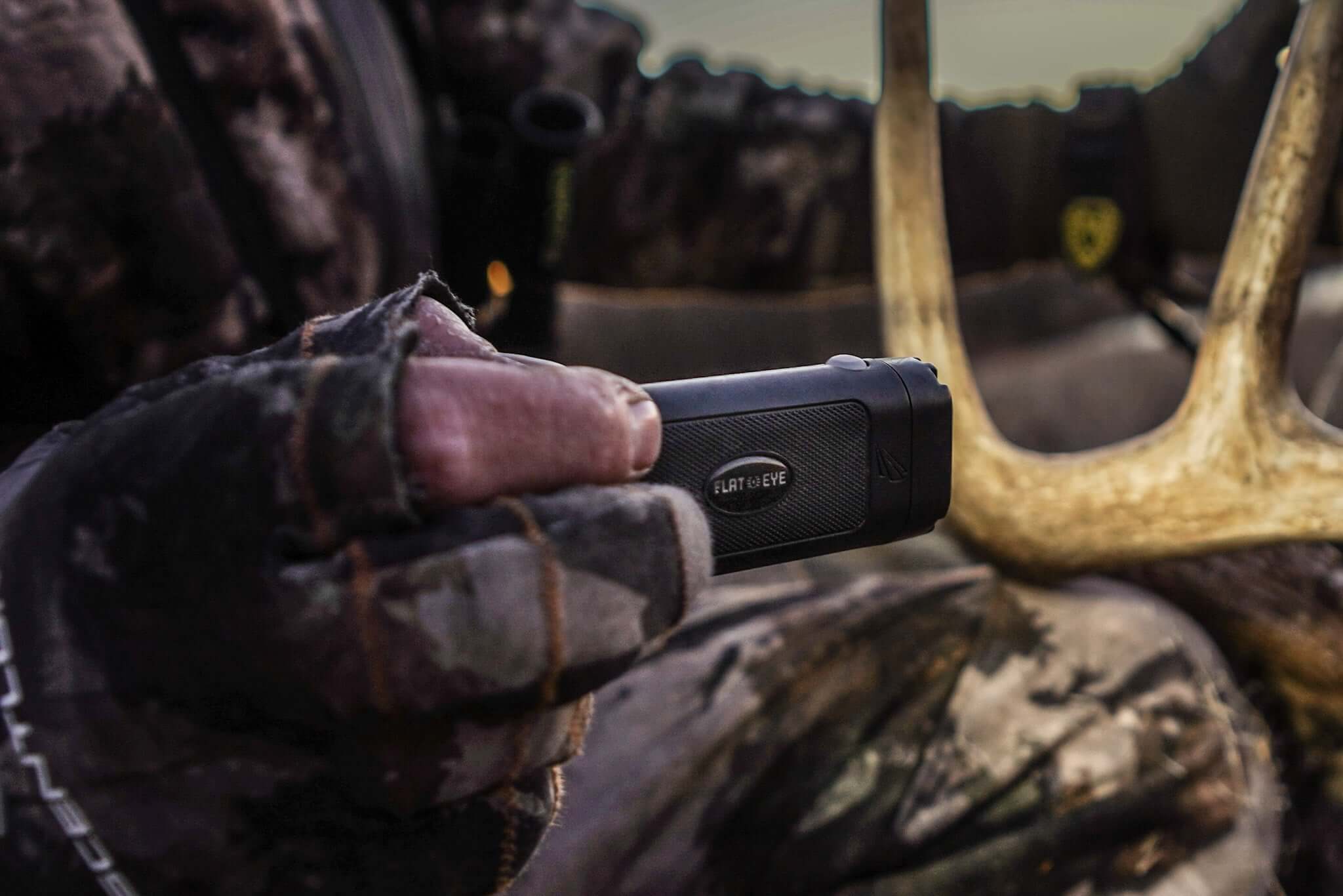 A gloved hand holding a compact flat-sided Panther Vision FLATEYE flashlight near antlers outdoors