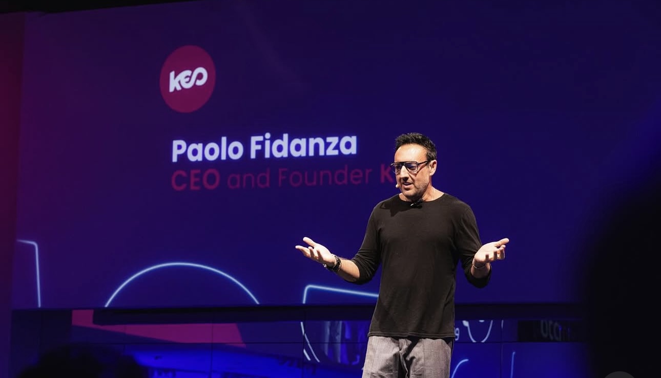 Paolo Fidanza speaking on a purple-lit stage with KEO branding behind him