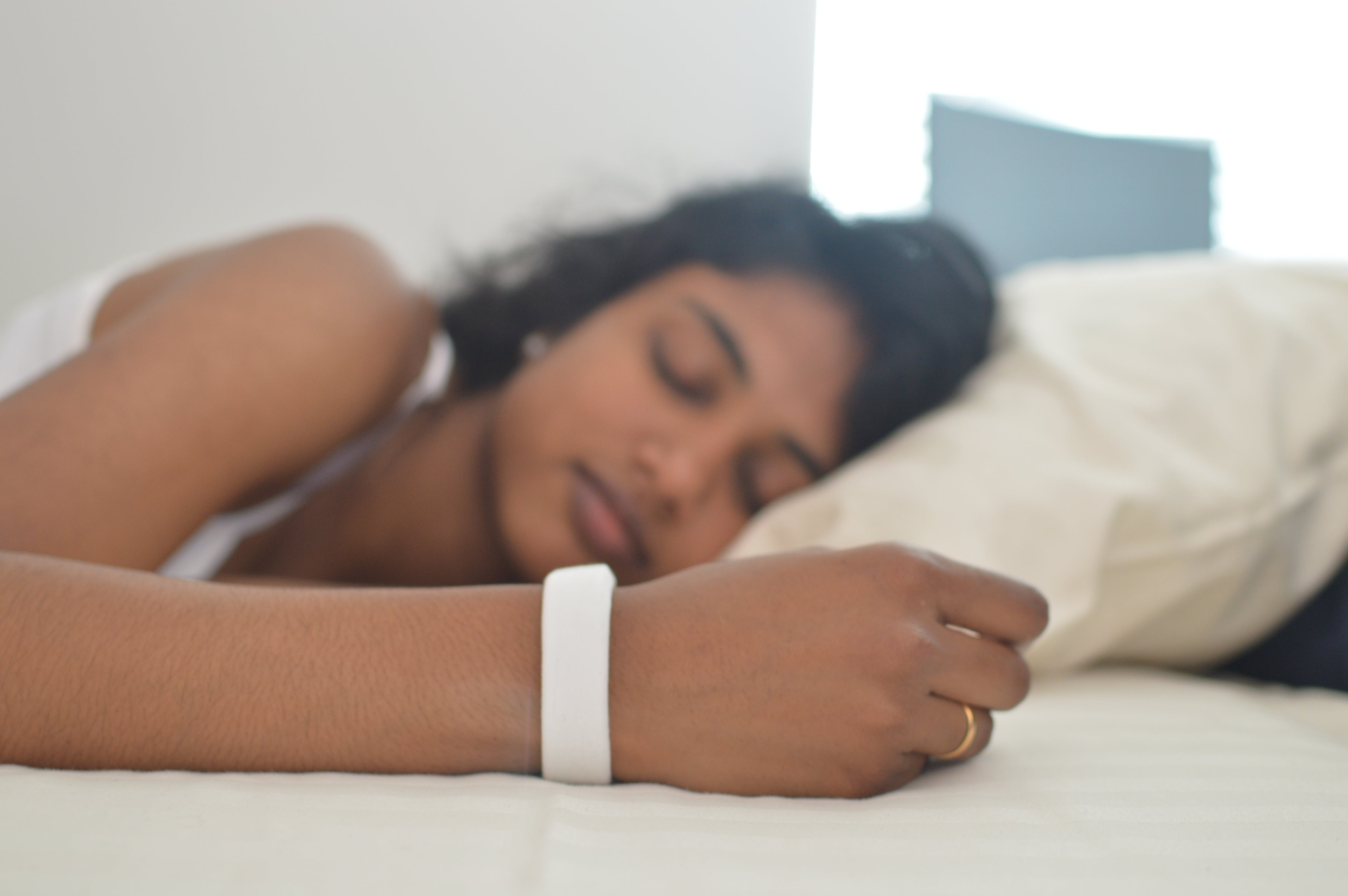 A person asleep in bed wearing a white VibeRise fabric band on the wrist