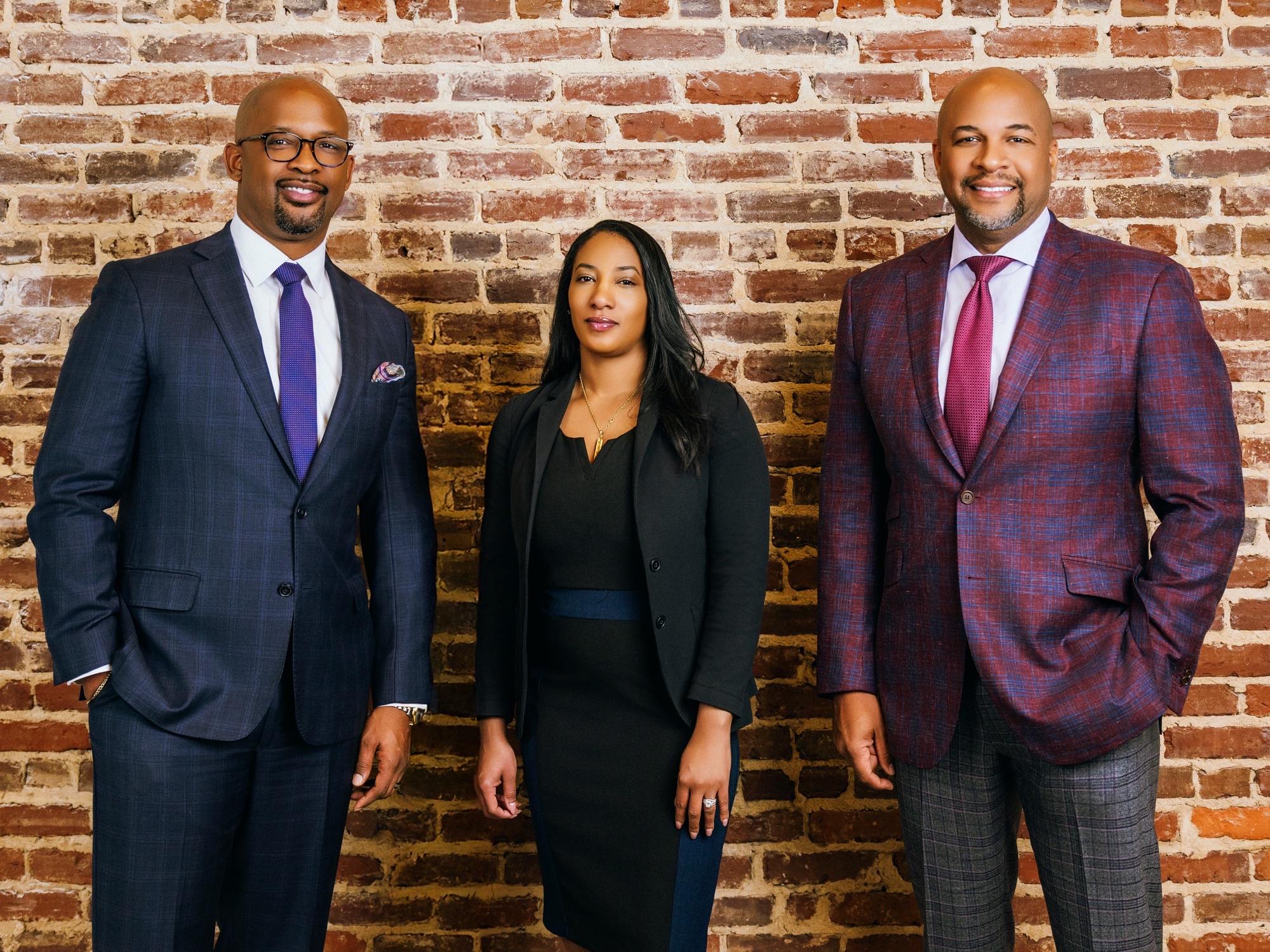 Three members of the Paramount Consulting Group team pose against a brick wall, with Tharon Johnson at right