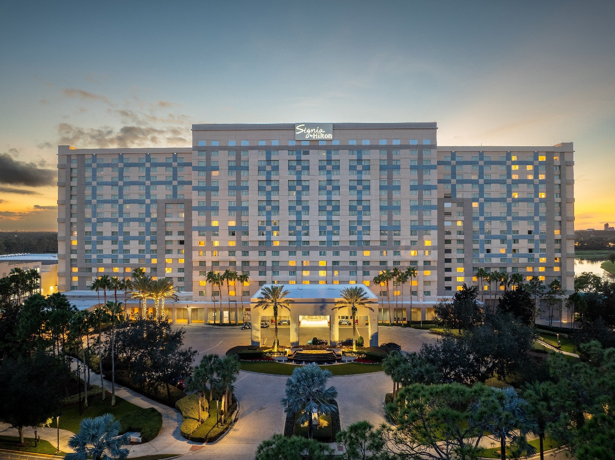 The illuminated Signia by Hilton Orlando hotel at dusk, with palm trees along its entrance