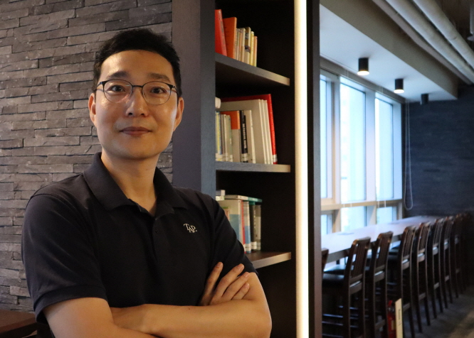 Park Jae Hyun wearing a TAP polo shirt beside bookshelves in an interview photograph