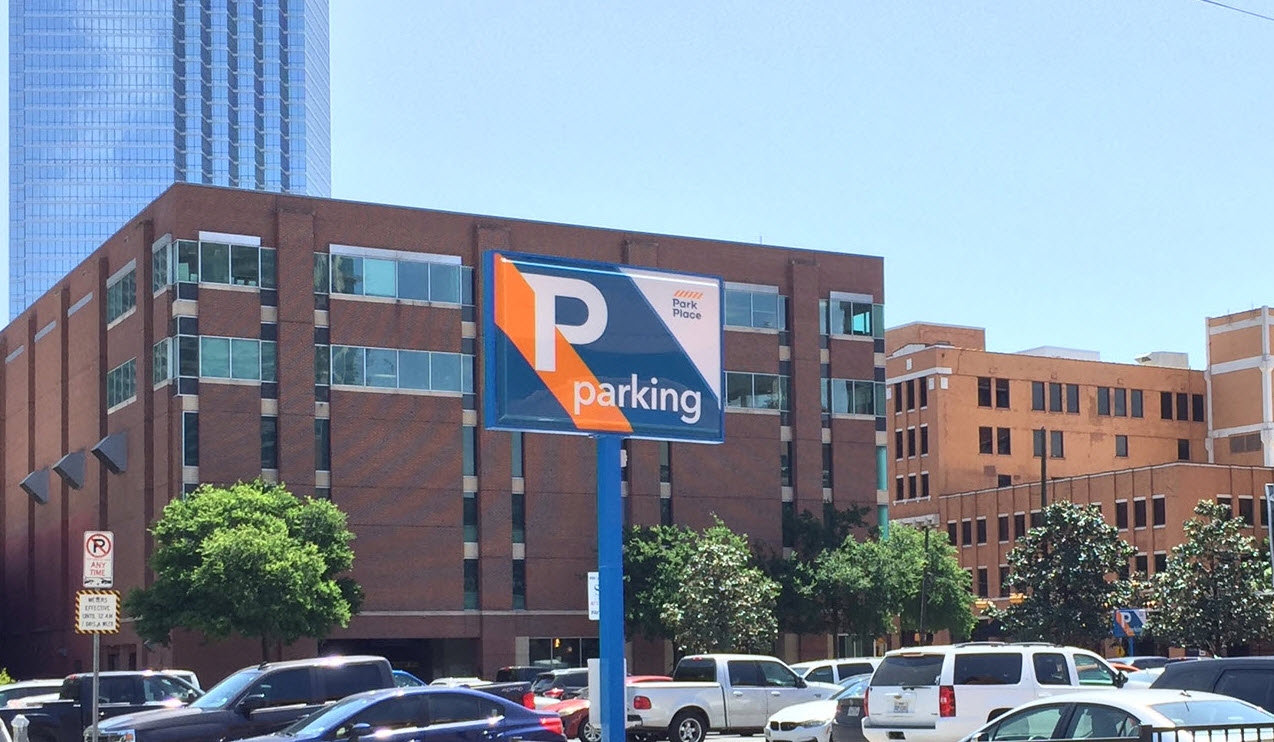 A blue and orange Park Place parking sign above cars on an urban lot