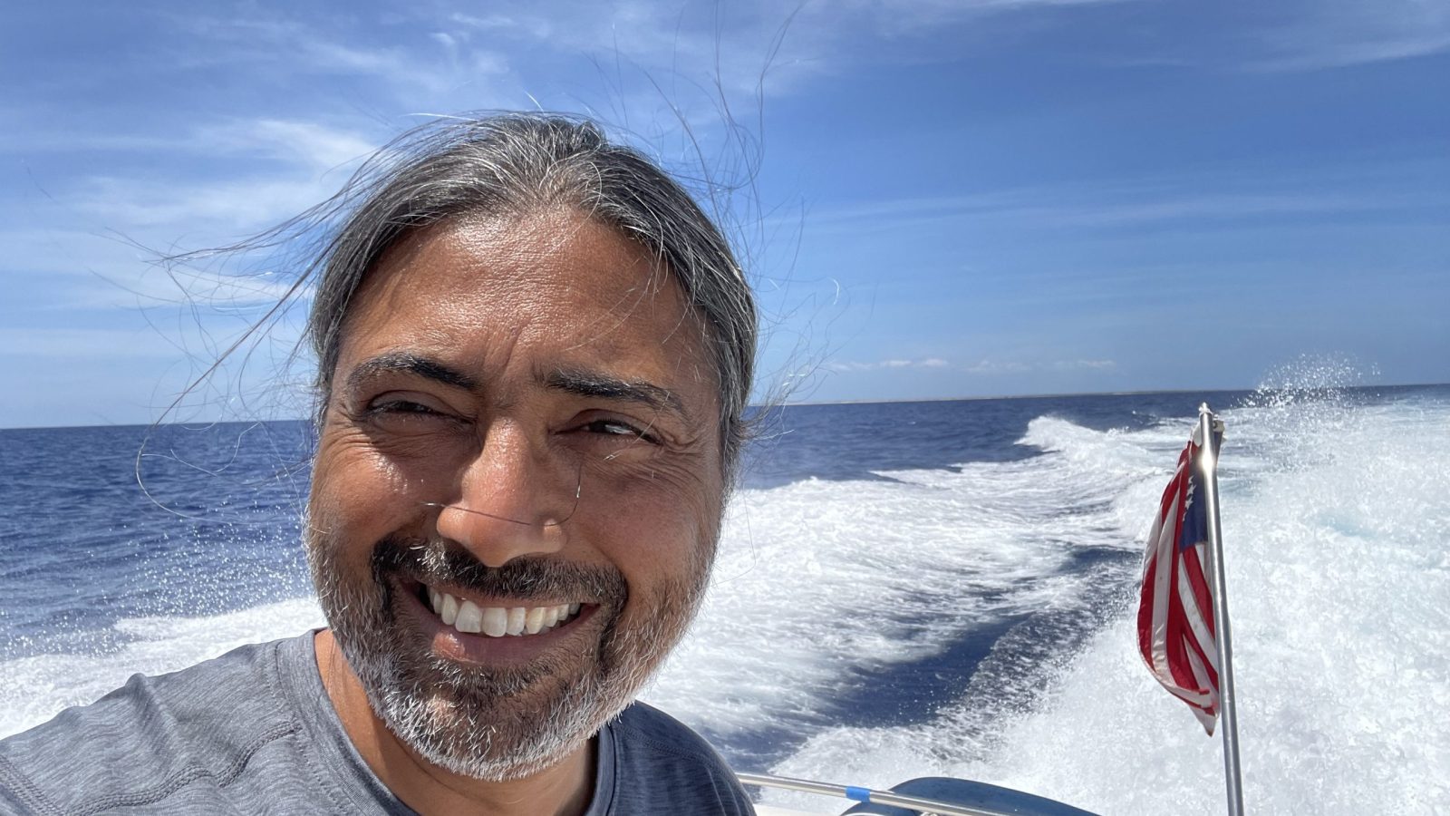 Parry Singh smiling aboard a boat, with open water and its wake behind him