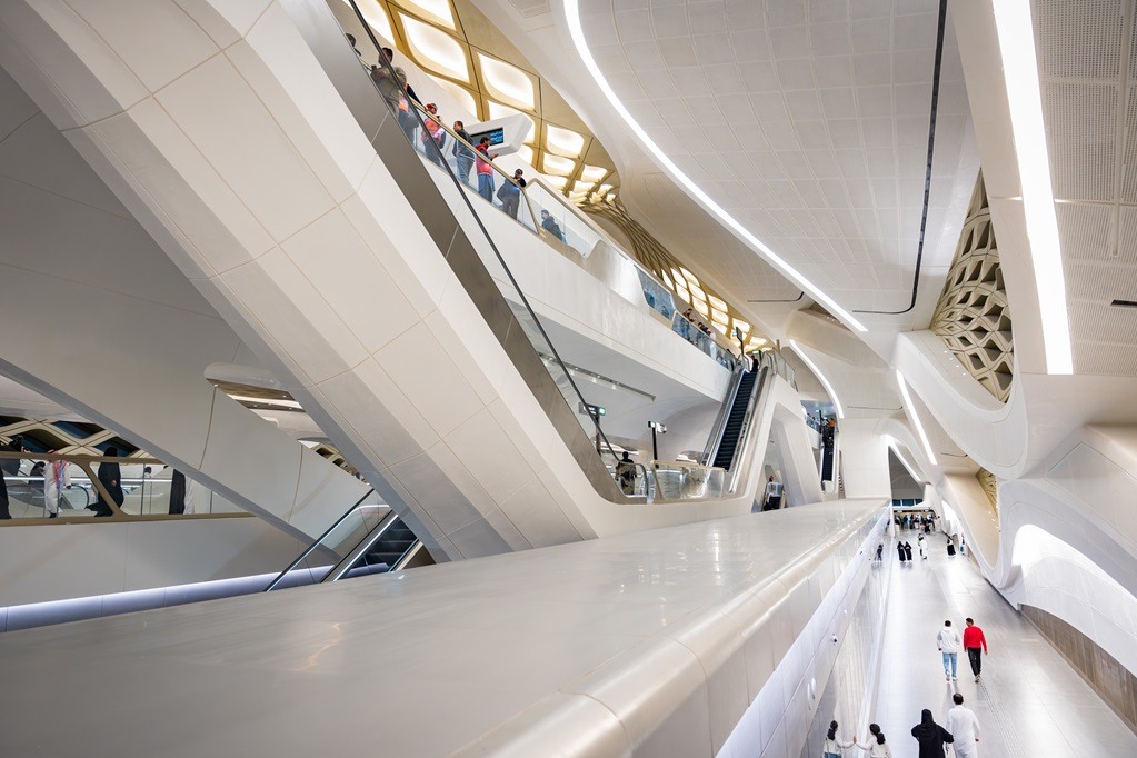 Passengers and escalators inside a sweeping white Riyadh Metro station
